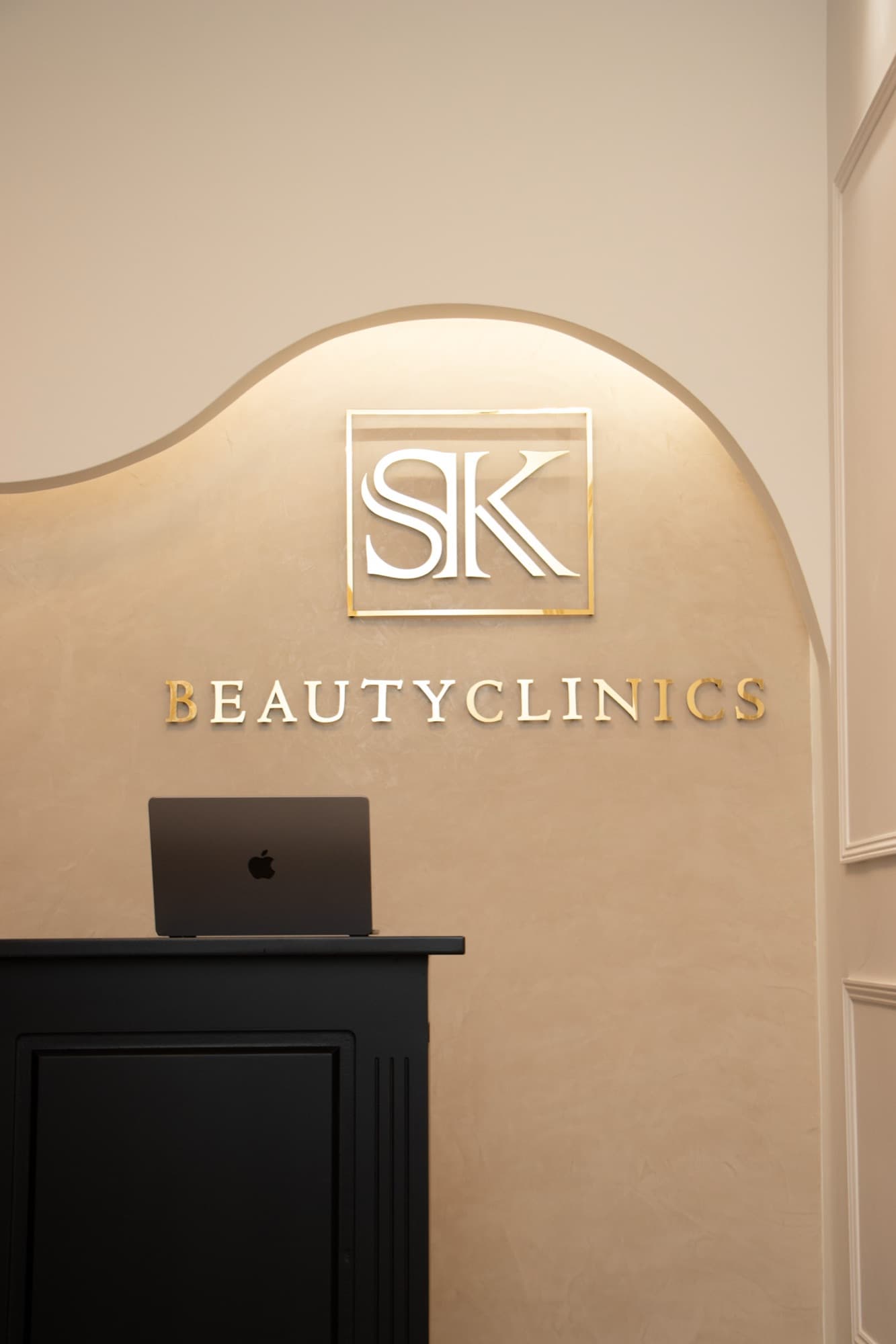Ontvangstbalie van SK Beautyclinics met het gouden SK-logo op de wand